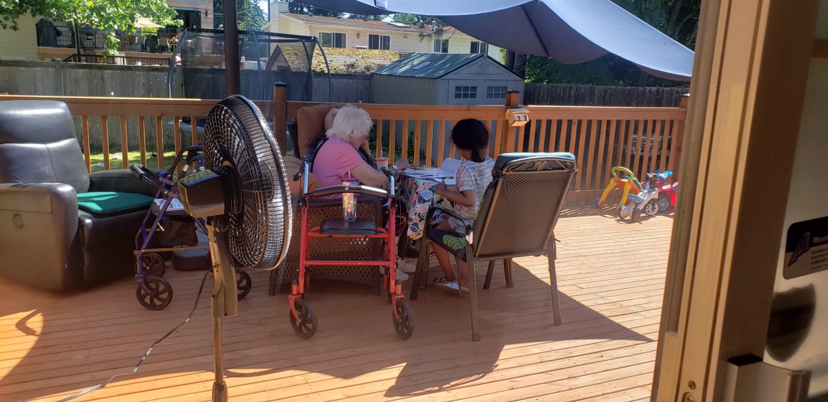 Two people sitting on a deck under a large umbrella, enjoying a sunny day.