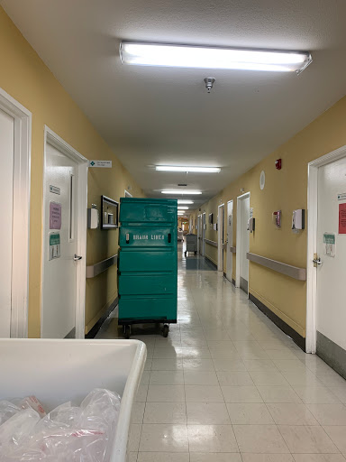 A view of a hospital corridor featuring a cleaning cart and patient rooms.