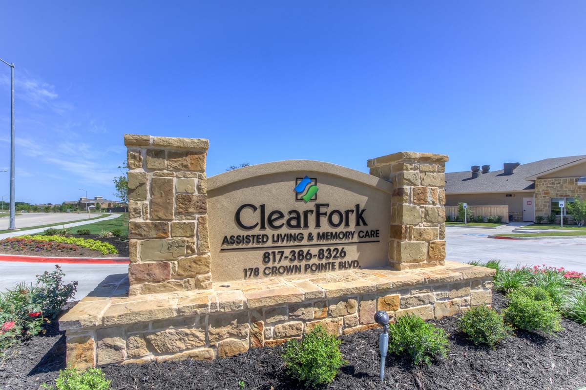 A stone sign for ClearFork Assisted Living & Memory Care with contact information, set against a clear blue sky.