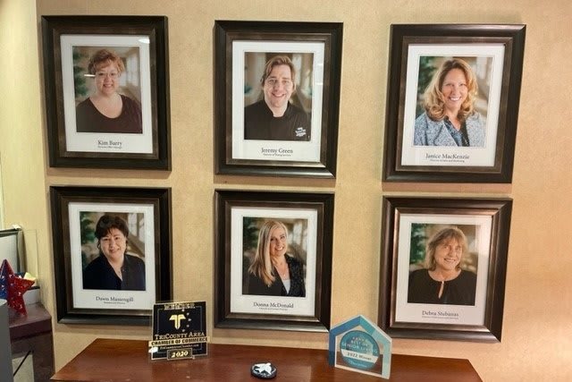 A collection of framed employee photos displayed on an office wall, with award plaques placed below.