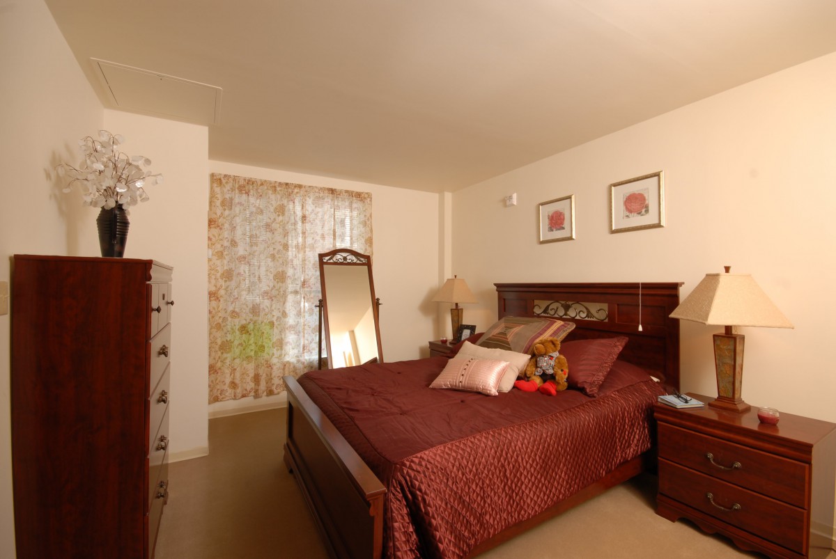 A cozy bedroom with a neatly made bed, standing mirror, and decorative elements.