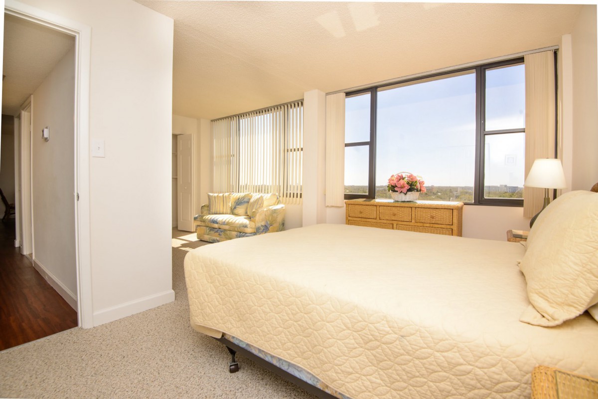 A bright and cozy bedroom with a large window, simple furnishings, and a comfortable atmosphere.