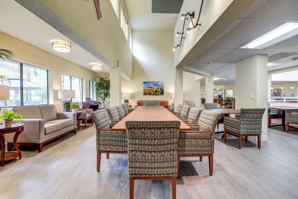A spacious, modern dining room with a long table and upholstered chairs, illuminated by ceiling lights.