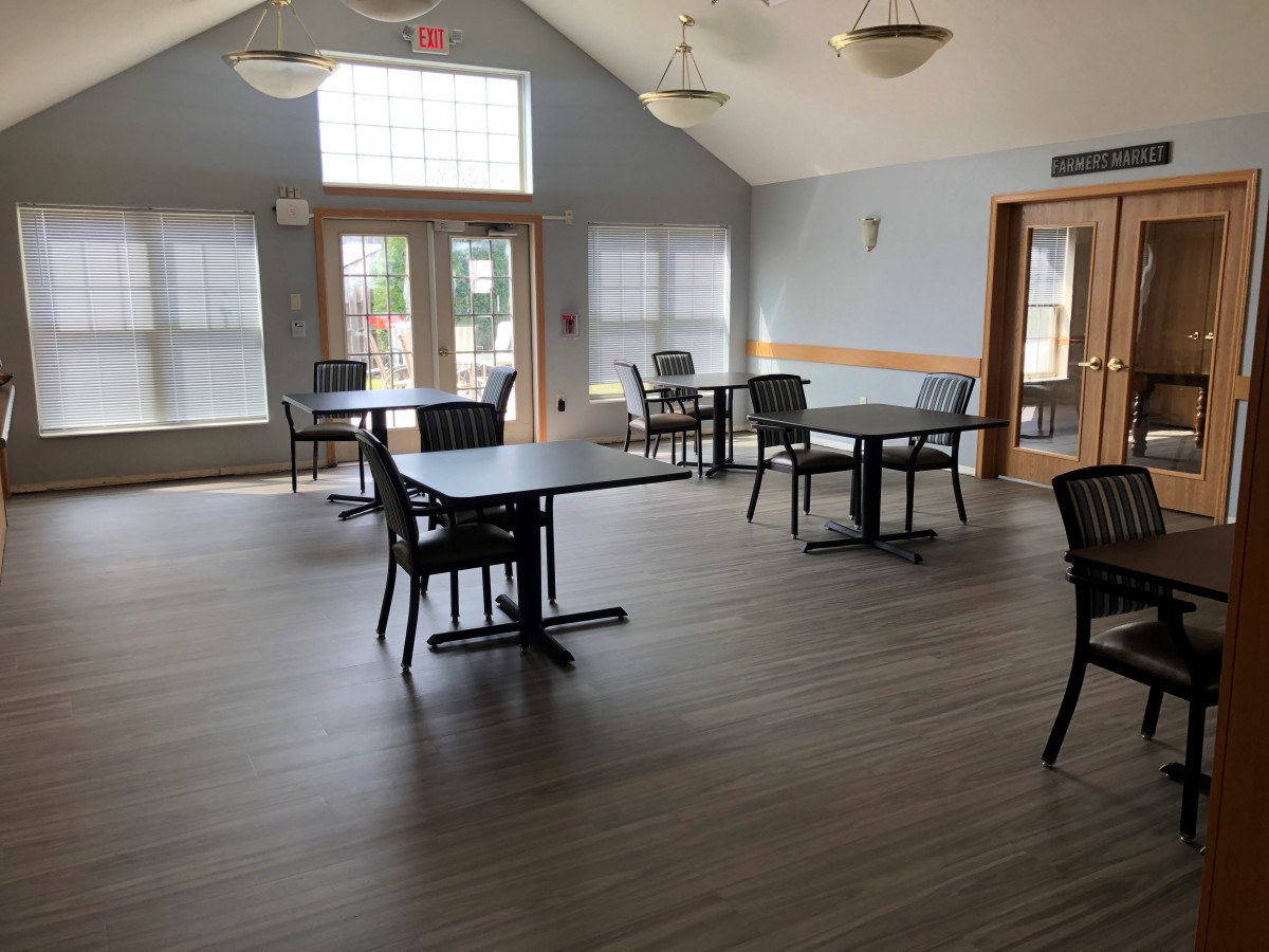 An empty indoor dining area with tables and chairs arranged on a wooden floor.