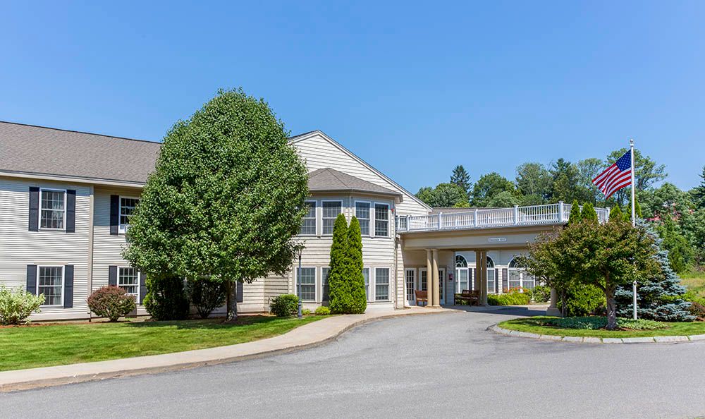 A two-story building with a covered driveway and surrounded by trees on a clear day.