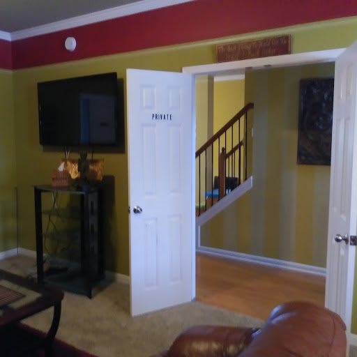 A cozy living room with a television, open door leading to a staircase, featuring yellow walls and a red accent wall.