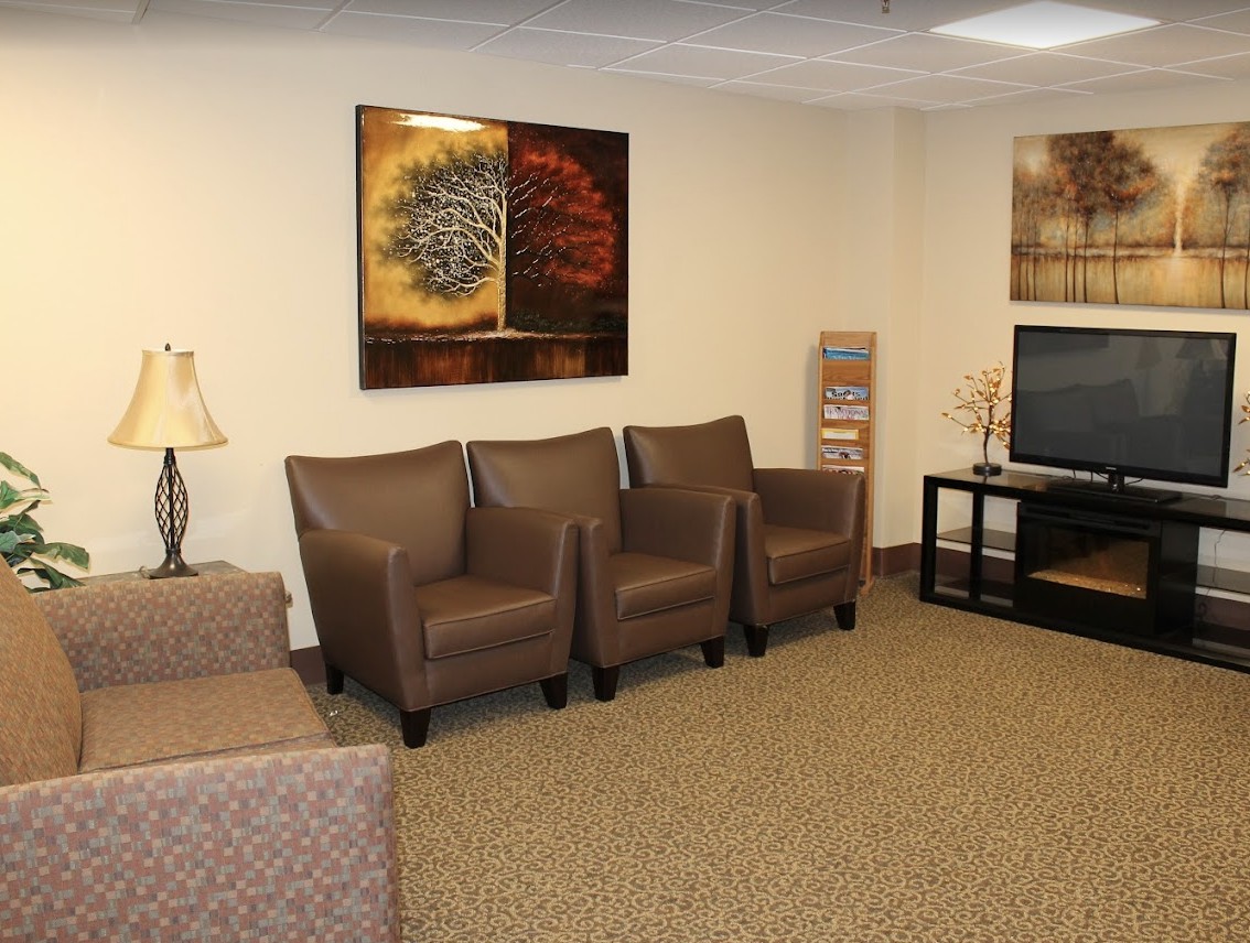 A cozy waiting room with chairs, a sofa, and a television.