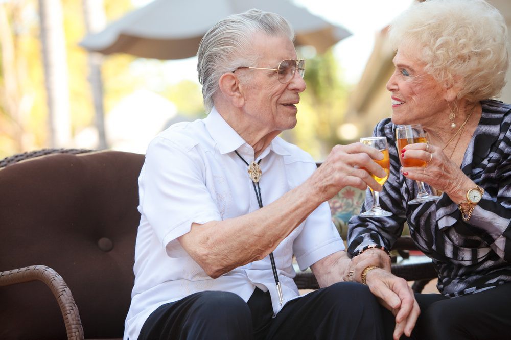 An elderly couple enjoying drinks and having a conversation outdoors.