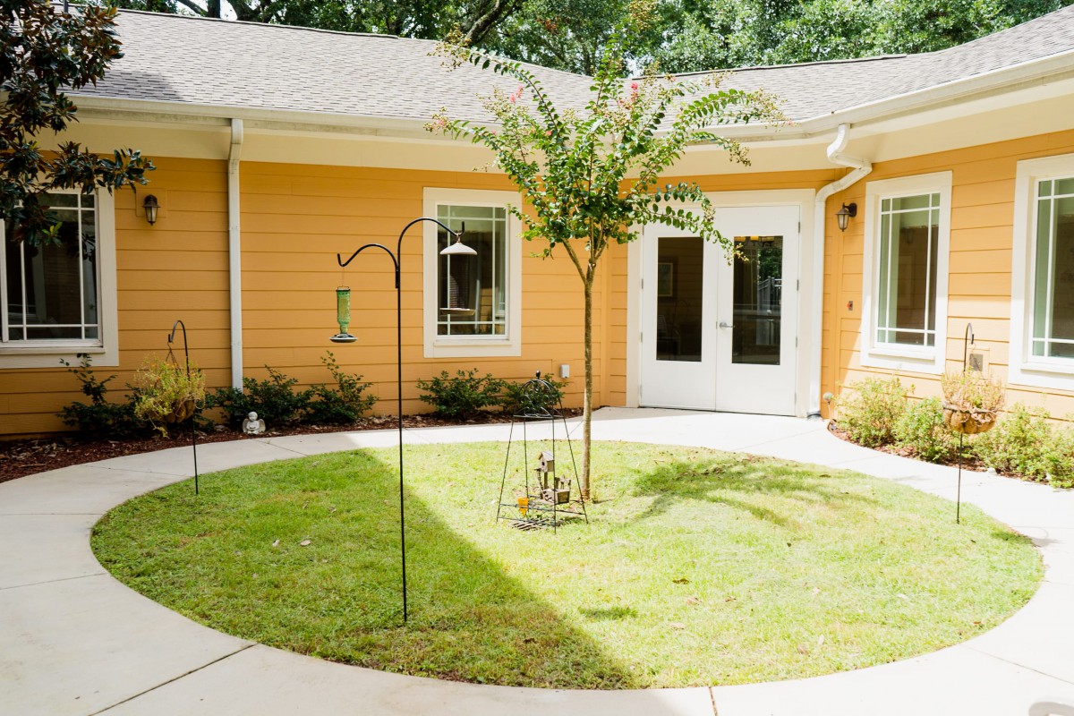 A cozy courtyard with a small tree and well-maintained lawn in front of a house with yellow siding.