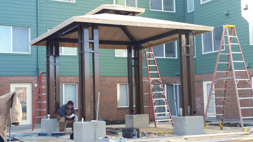 A partially constructed pavilion with a worker on-site, surrounded by scaffolding and building materials.