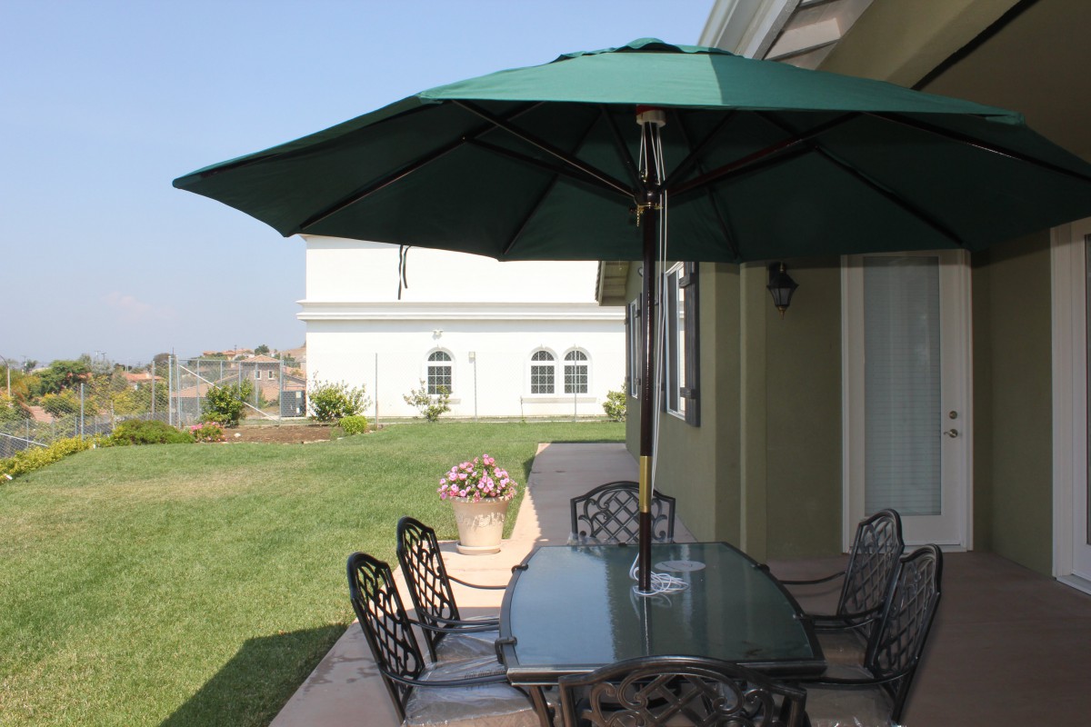 A cozy patio setup with a glass table, chairs, and a large green umbrella in a backyard.