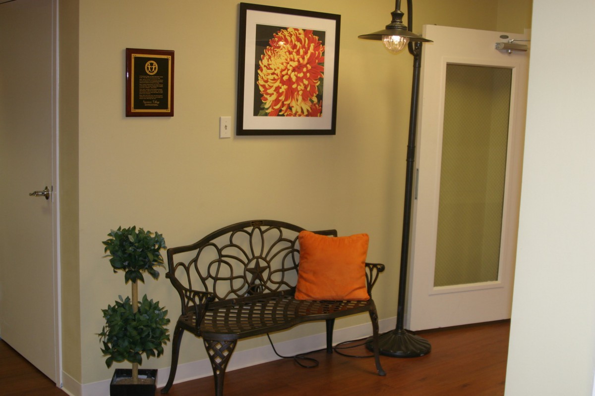 A cozy corner with a decorative bench, an orange pillow, wall art, and a standing lamp.