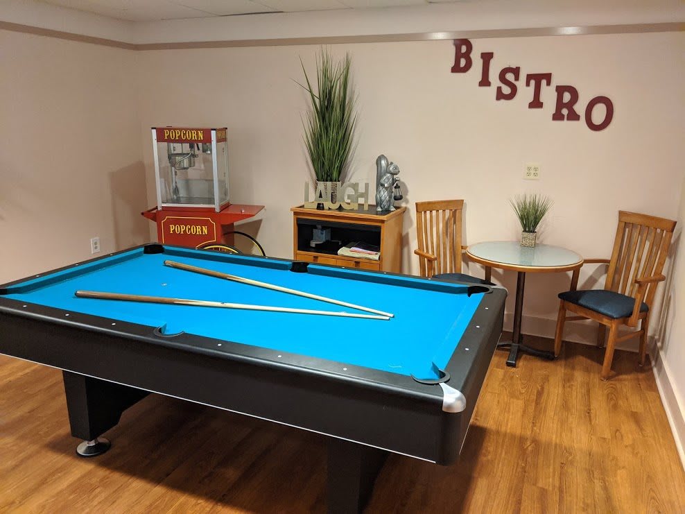 A cozy game room featuring a pool table with blue felt, a popcorn machine, and bistro decor.