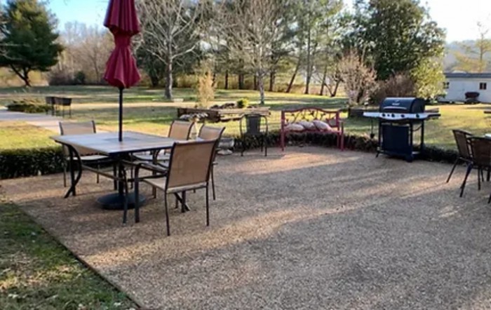 A cozy backyard patio with a dining set, umbrella, and grill overlooking a scenic landscape.