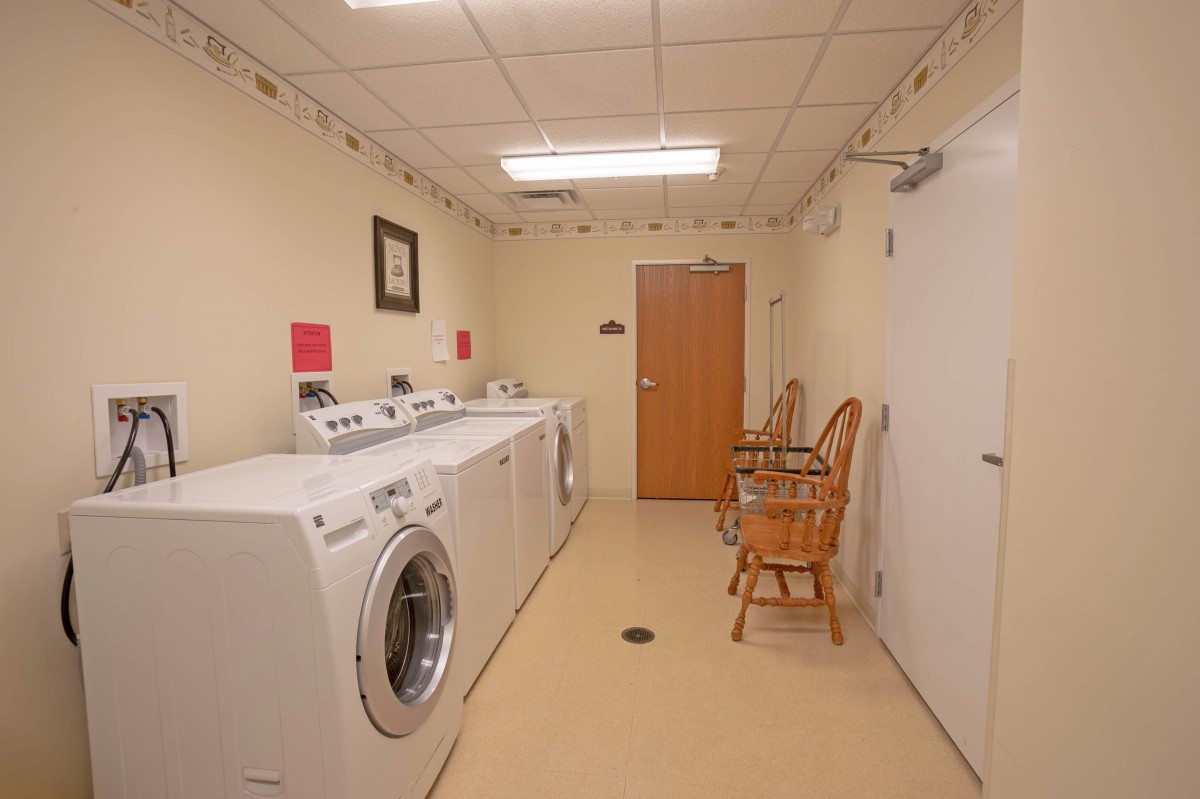 A clean and organized laundry room with washing machines and chairs.