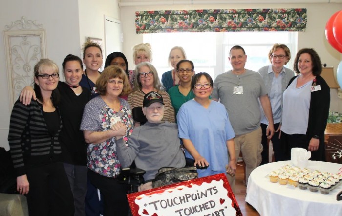 A diverse group of people gathered indoors, celebrating with a cake.