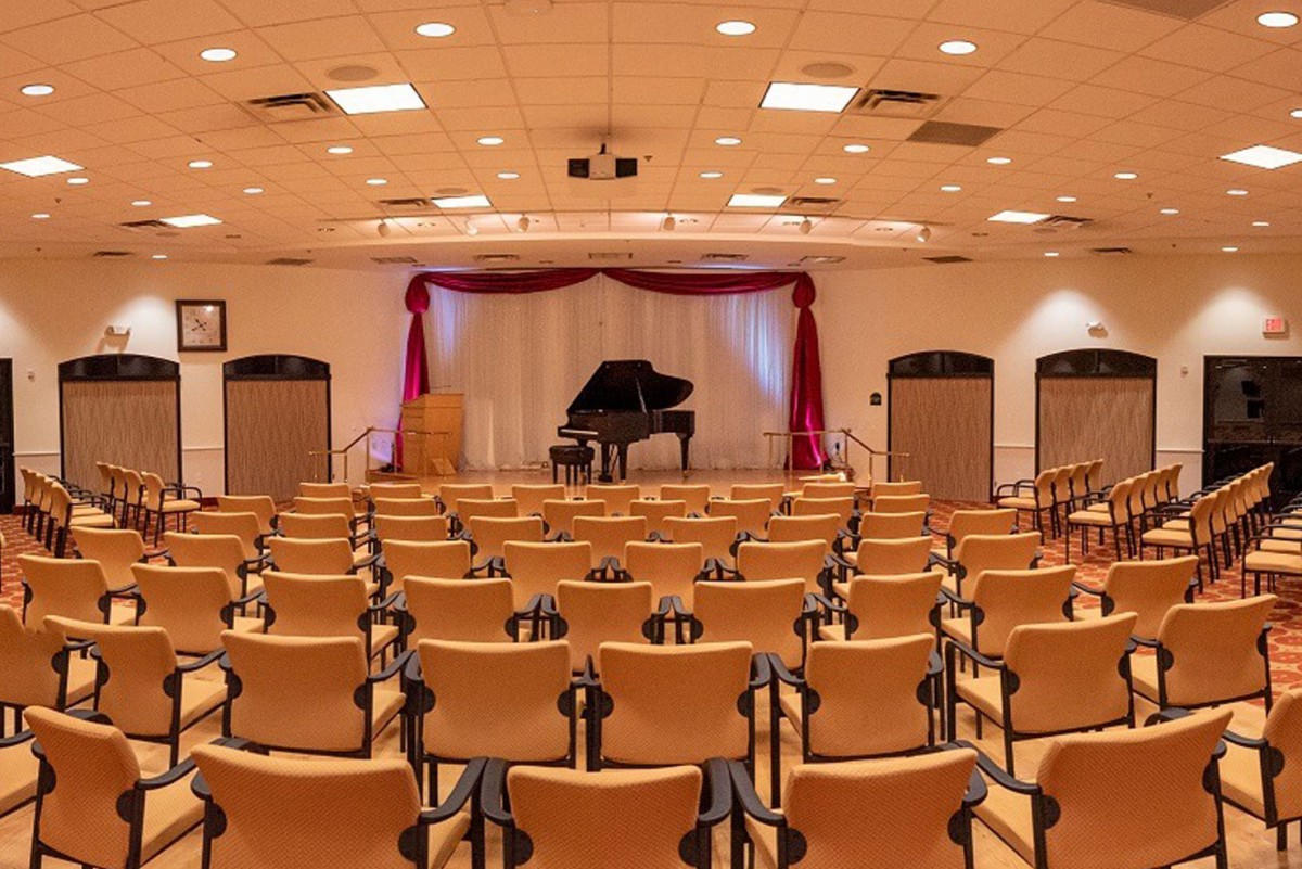 An empty concert hall with a grand piano on stage and rows of chairs facing the performance area.