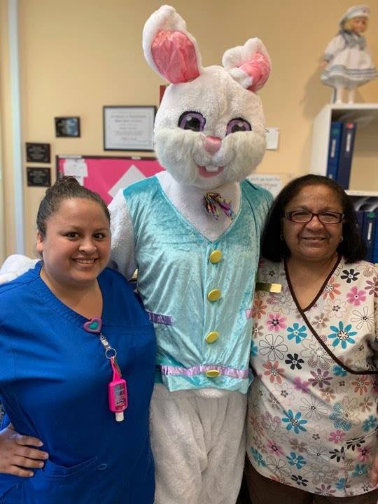 Two people posing with a person in a bunny costume indoors.