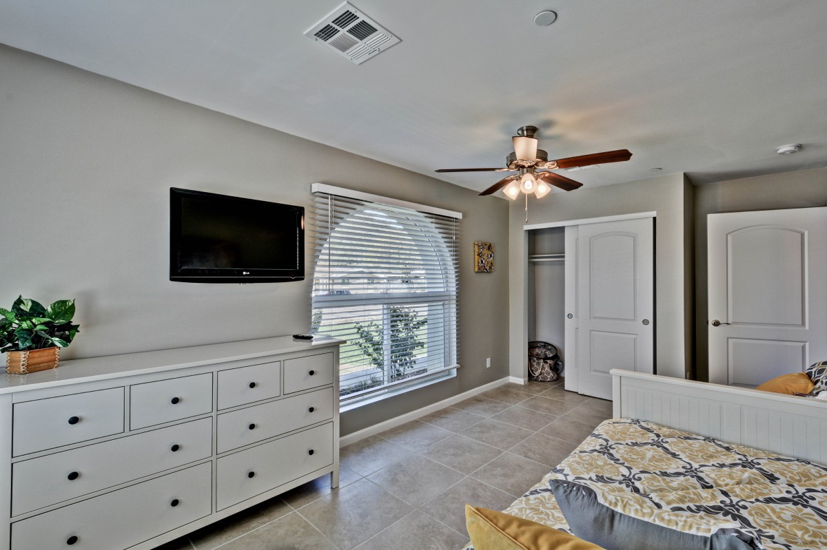 A modern bedroom with a dresser, bed, ceiling fan, and flat-screen TV.