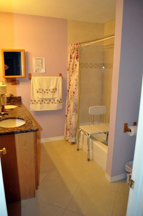 A bathroom with a sink, mirror, and shower featuring a bath seat and floral curtain.