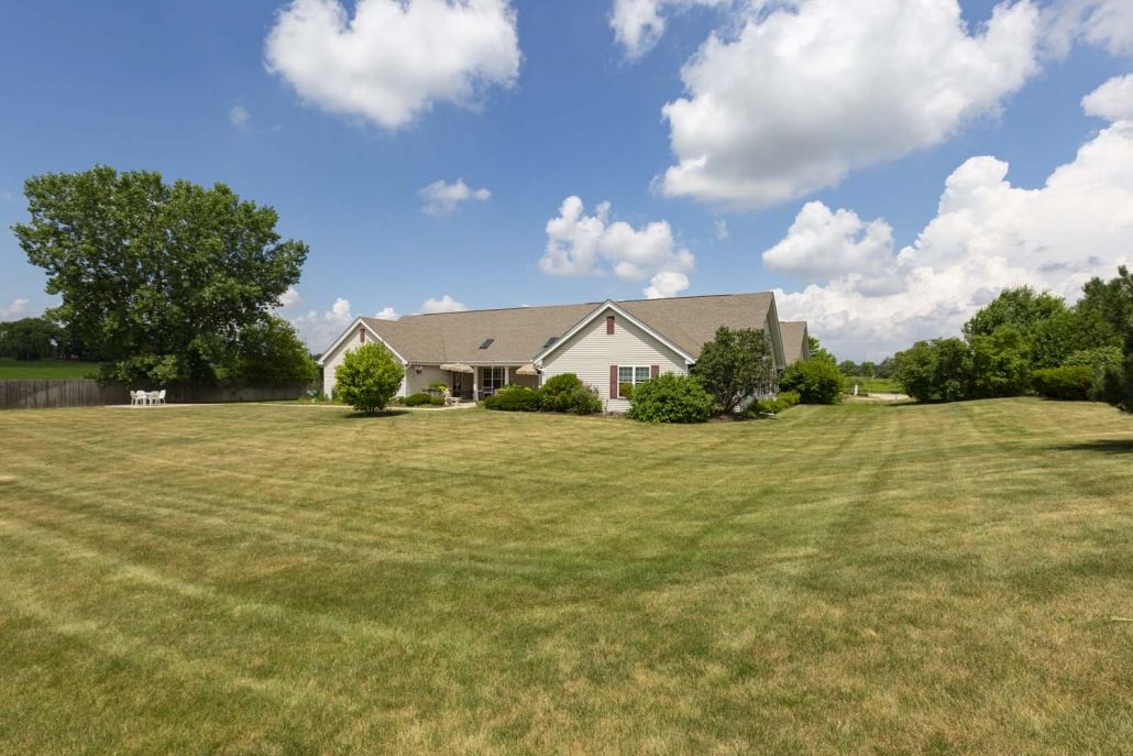 A suburban house with a large, well-maintained lawn under a partly cloudy sky.