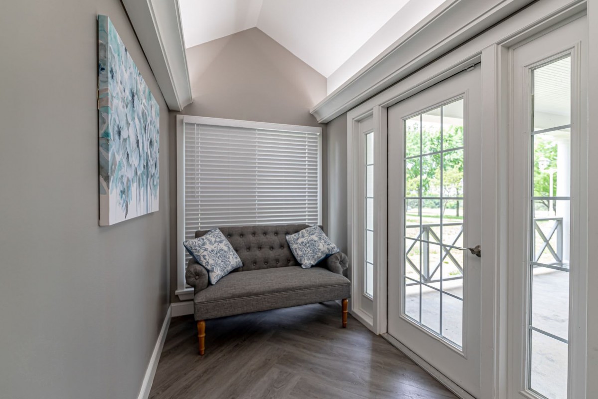 A cozy corner with a small sofa and decorative pillows near large windows and glass doors.