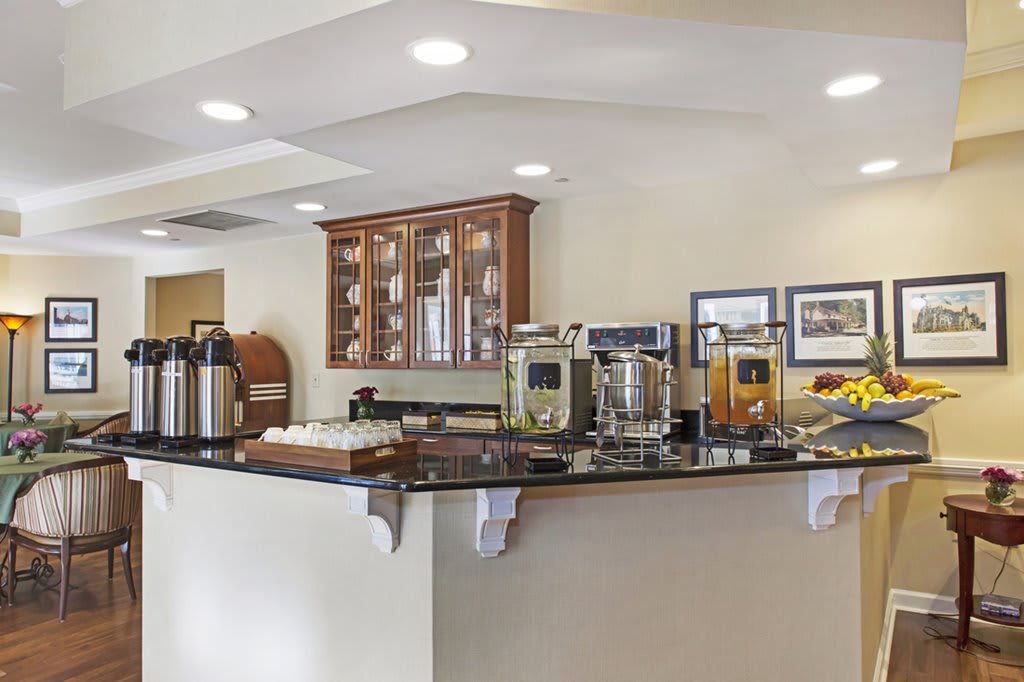 A hotel breakfast area featuring a self-serve buffet with coffee and juice dispensers.