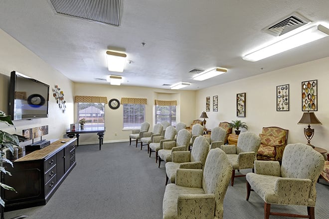 A spacious waiting room with rows of cushioned chairs, well-lit by overhead lighting and natural light from large windows.