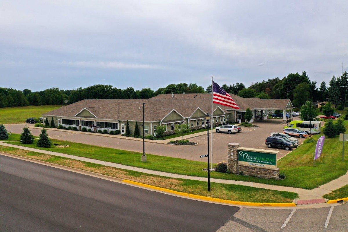 A large building with an American flag in front, adjacent to a parking lot and a road.