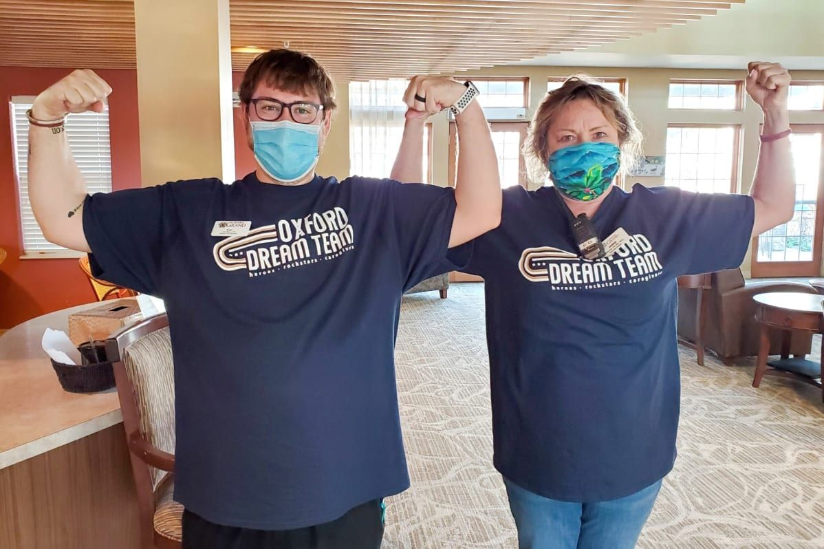 Two people wearing matching t-shirts and masks, smiling indoors.
