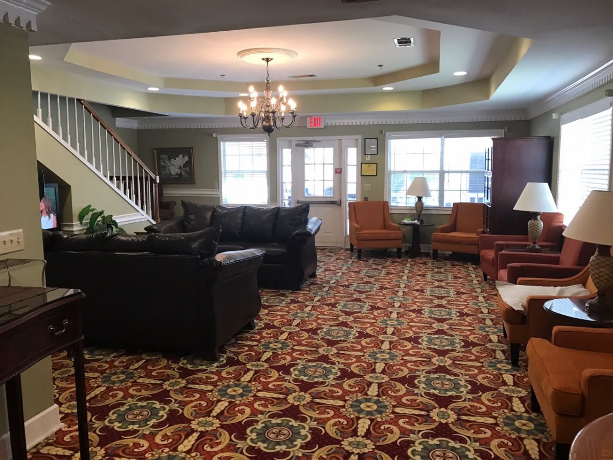 A cozy living room with patterned carpeting, sofas, and a chandelier.