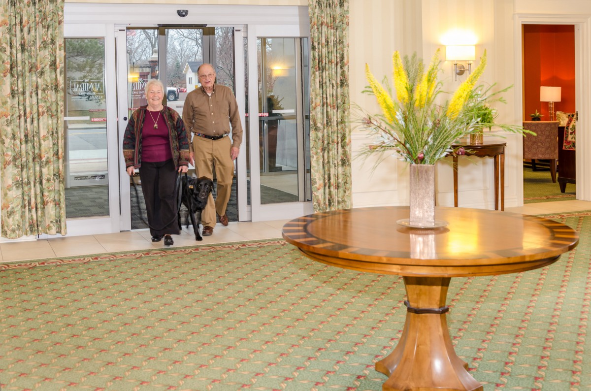 An elderly couple walking into a hotel lobby with a flower arrangement on display.