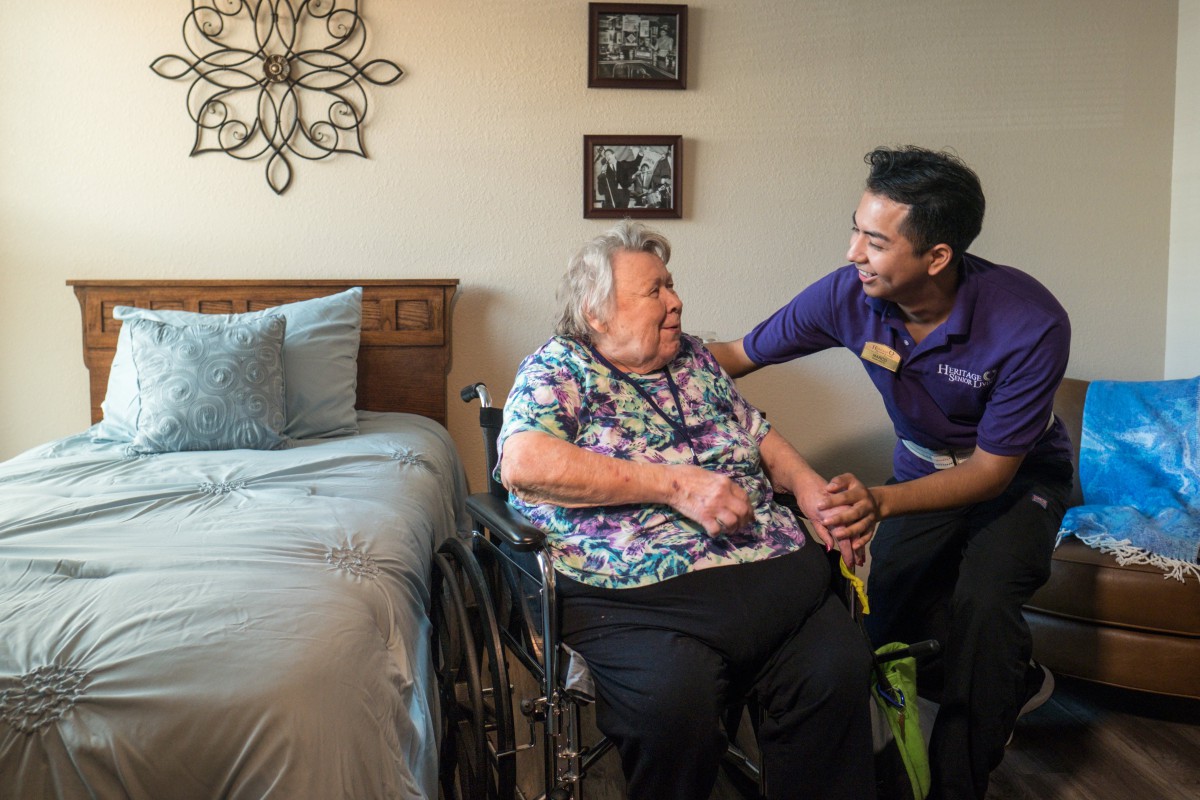 A caregiver interacts with an elderly woman in a nursing home setting, providing support and companionship.