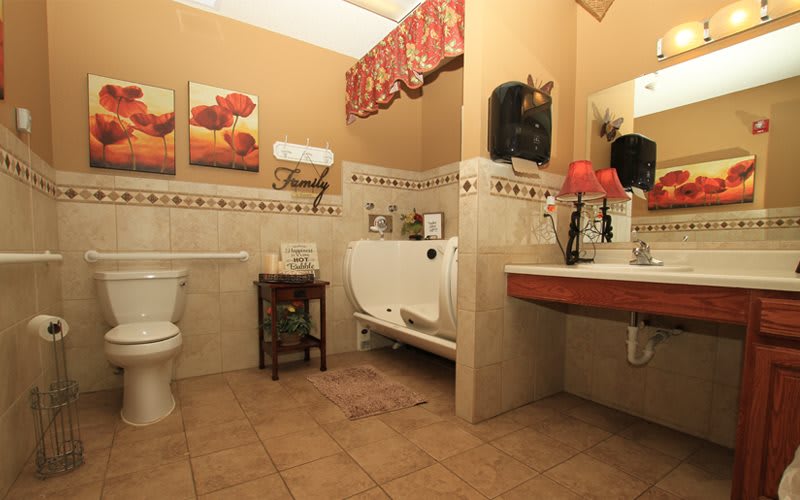 A warmly decorated bathroom featuring a bathtub, toilet, and sink with a tiled floor and wall art.