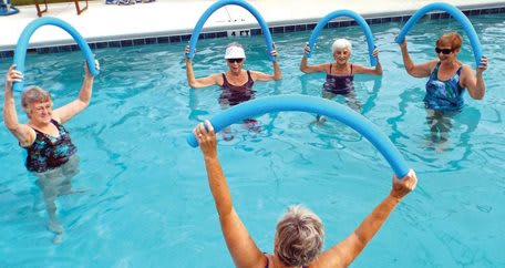 A group of seniors participating in a water aerobics class using pool noodles.
