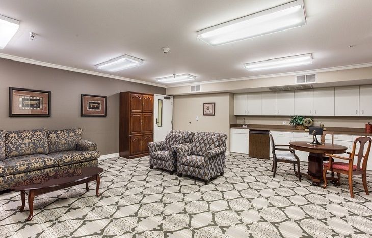 A modern living space with a patterned carpet, comfortable seating, and a kitchenette.