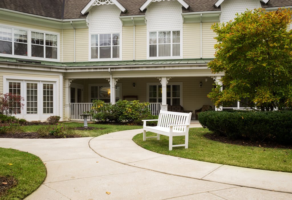 A charming house with a landscaped front yard featuring a white bench and a curved pathway.
