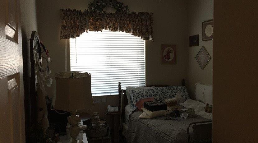 A cozy bedroom with a bed, lamp, and window with blinds.