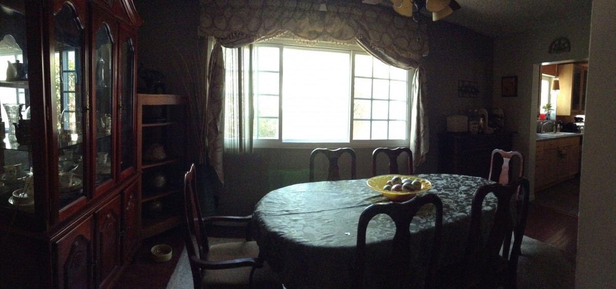 A dining room with a table and chairs, softly lit by natural light through a large window.