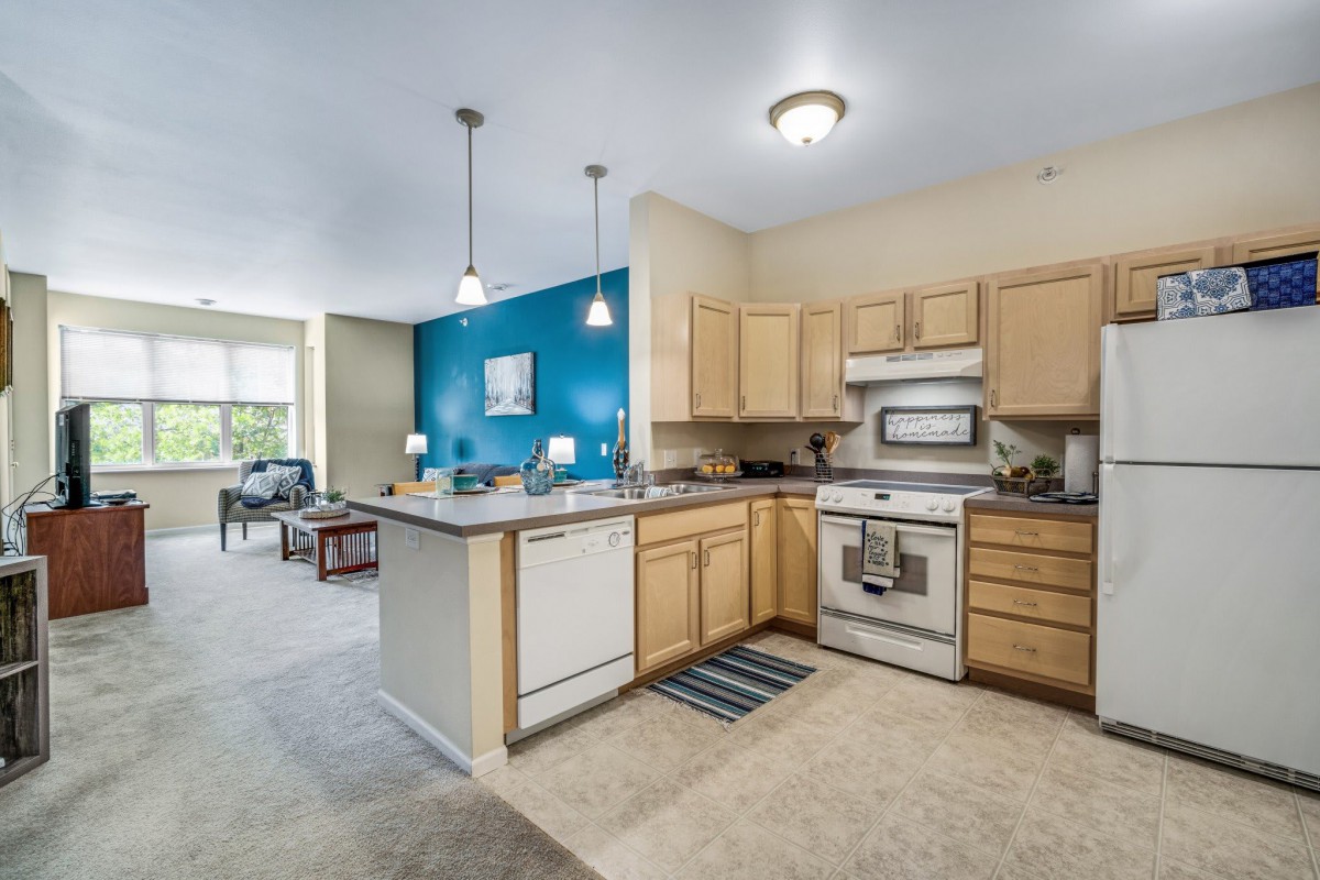 A modern open-layout kitchen with wood cabinets and bright lighting, connected to the living room area.