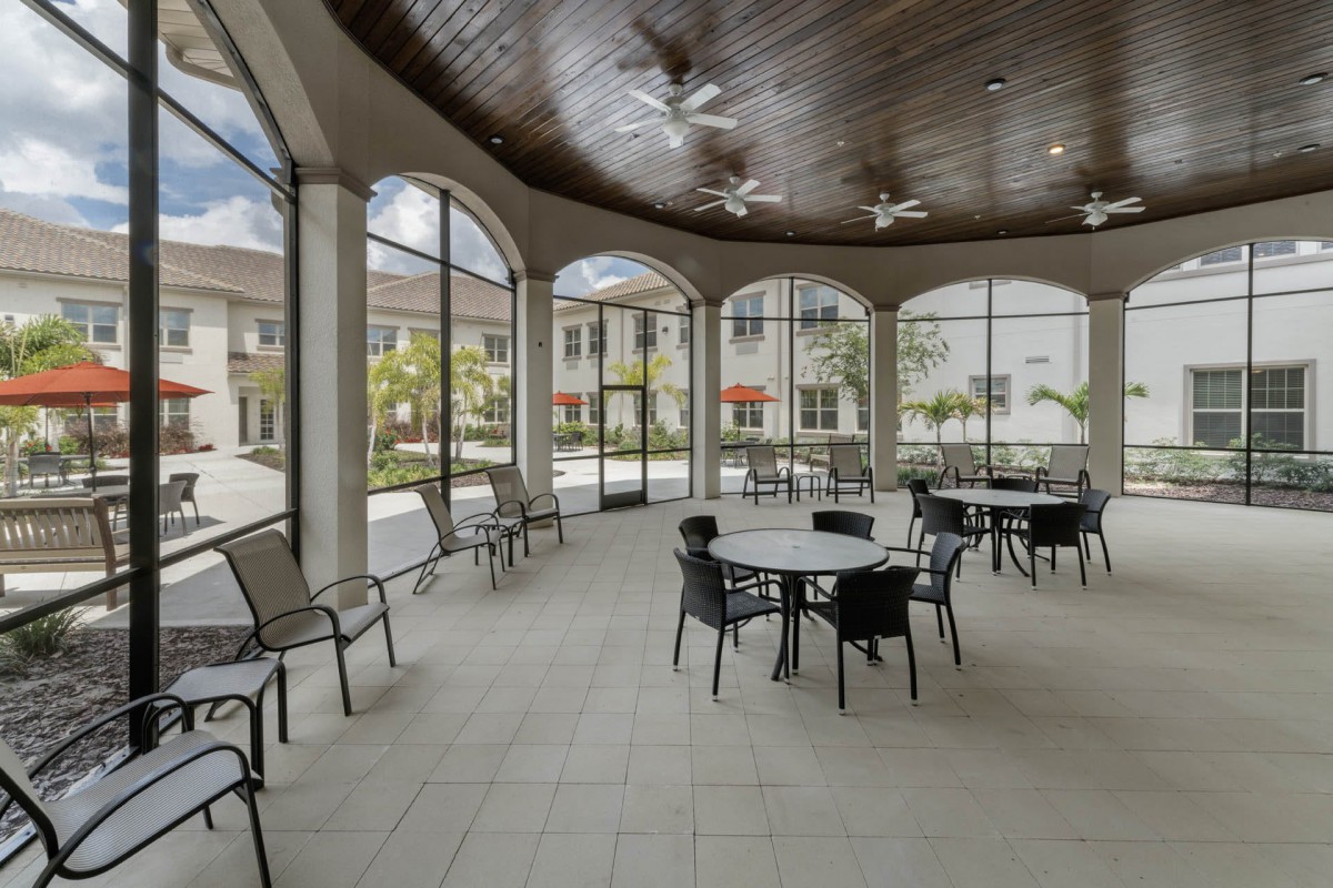 A bright indoor patio area with tables and chairs, surrounded by large arched windows.