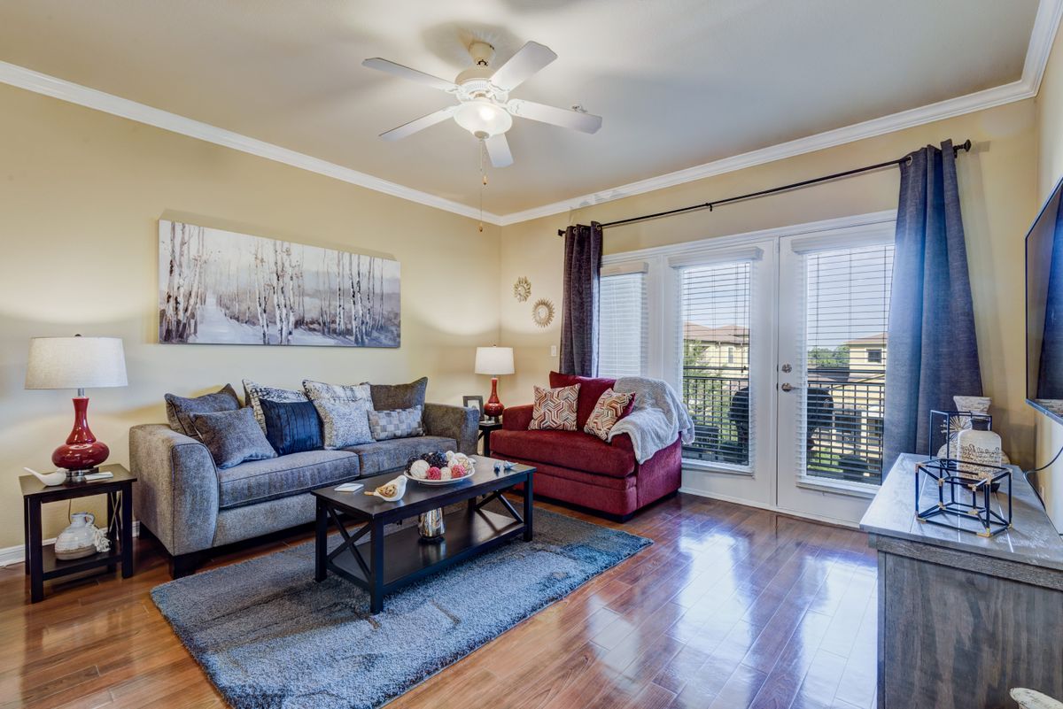 A cozy living room features a comfortable sofa and armchair, with a coffee table on a rug. Natural light streams through large glass doors, illuminating the hardwood floors and tasteful decor.