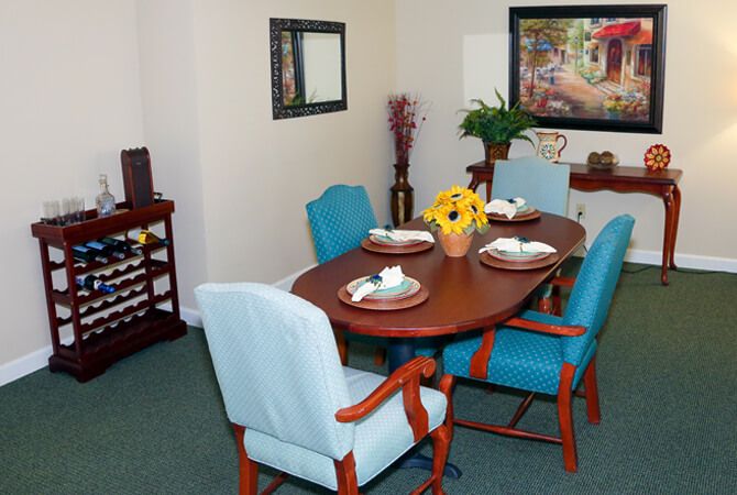 A cozy dining room with a wooden table set for four, featuring light blue chairs and a centerpiece of vibrant yellow flowers.