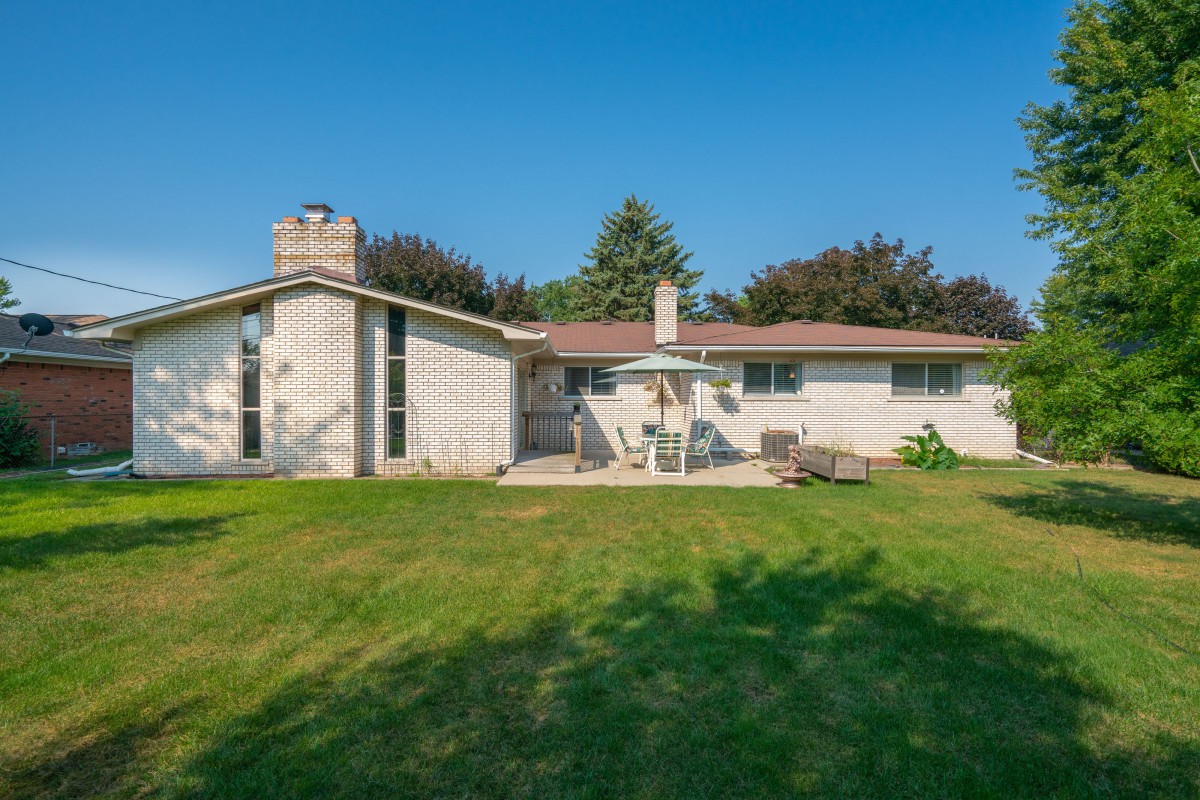 A sunny backyard view of a single-story house with a patio and lawn.