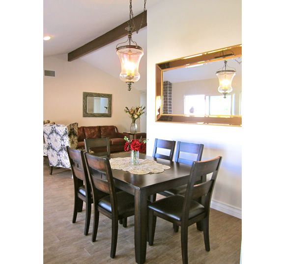 A cozy dining room with a wooden table and chairs, accented by a hanging light fixture and a large mirror on the wall.