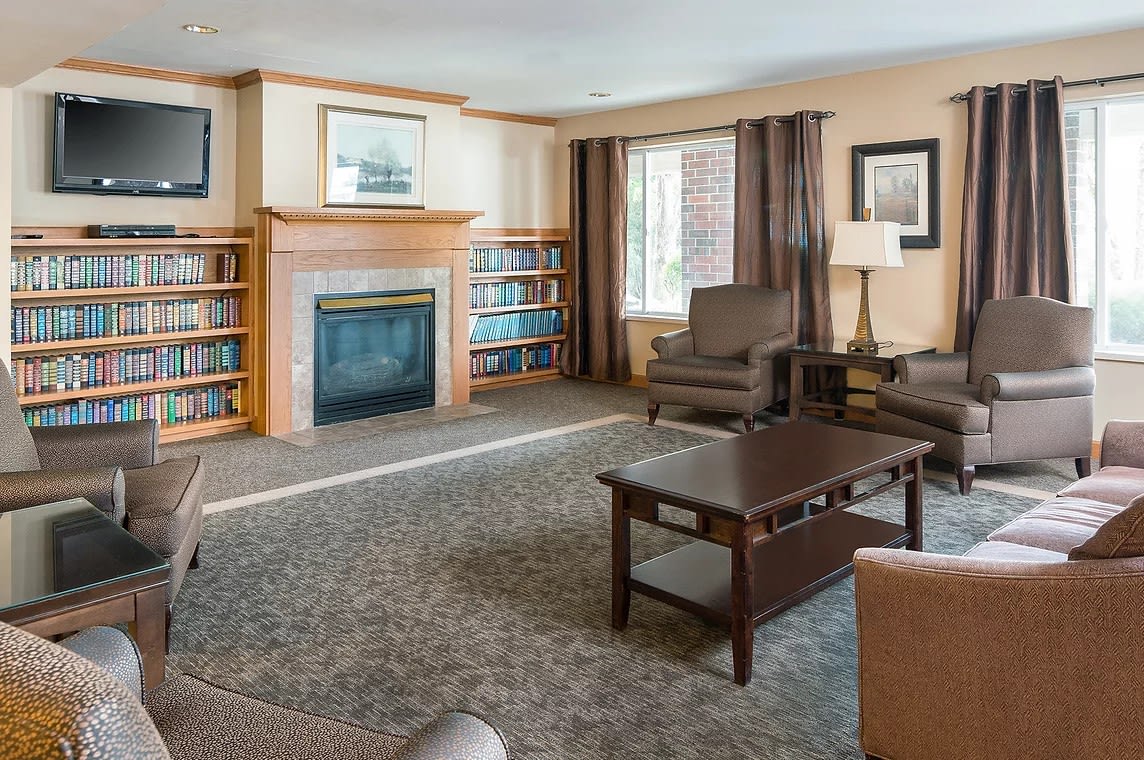 A cozy living room with a fireplace and bookshelves, featuring comfortable furniture and soft lighting.