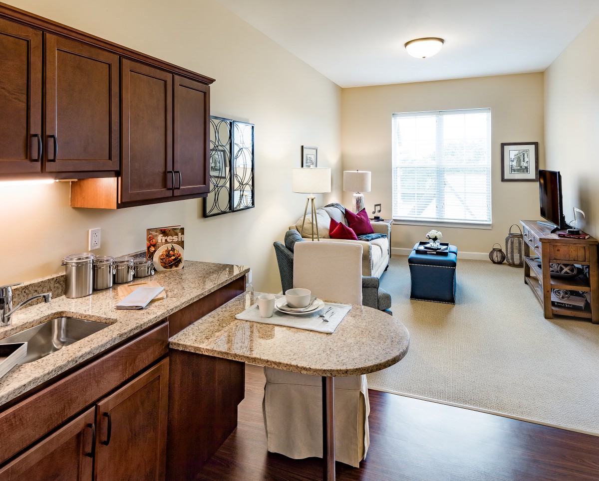 A cozy open-concept kitchen and living room with wooden cabinets and a bright window.
