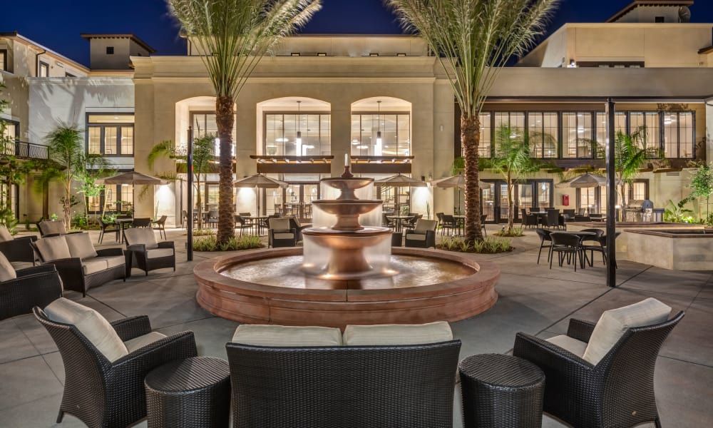 A modern outdoor courtyard with a central fountain surrounded by seating, illuminated at night.