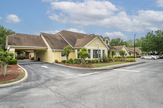 A single-story residential building with a landscaped front and a driveway, under a partly cloudy sky.