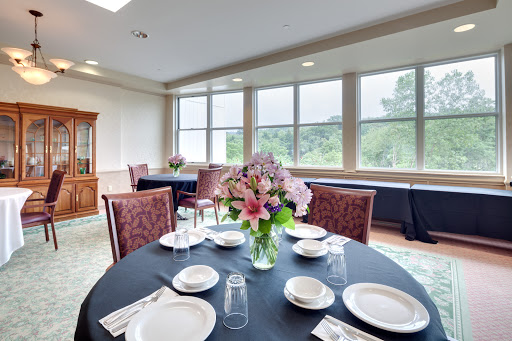 An elegantly set dining table with a beautiful floral centerpiece, surrounded by large windows that offer a scenic view.